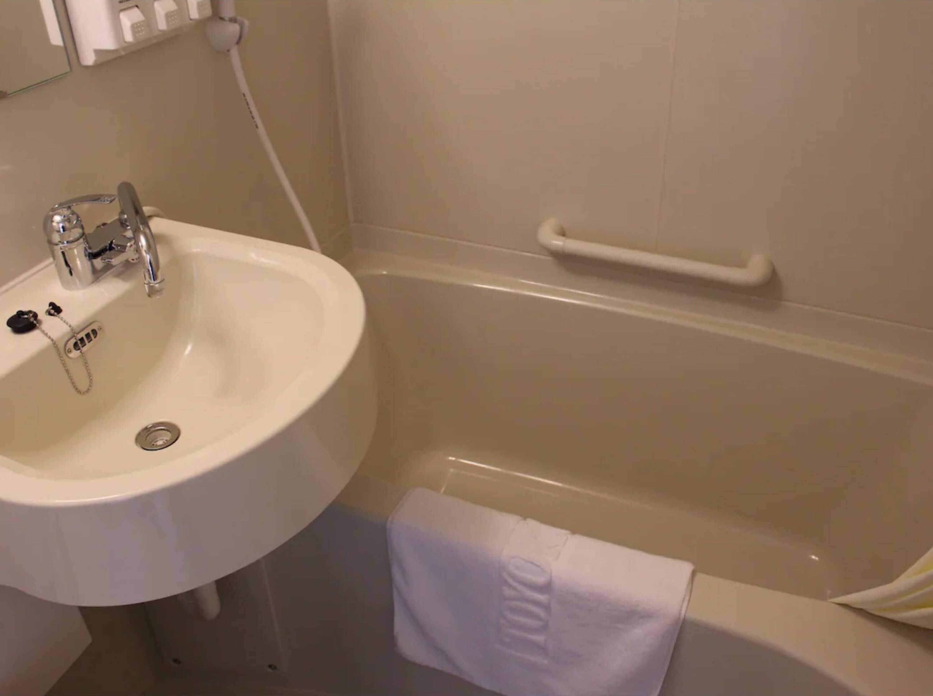 A bathroom with a white sink, a bathtub, and a towel hanging on the wall.