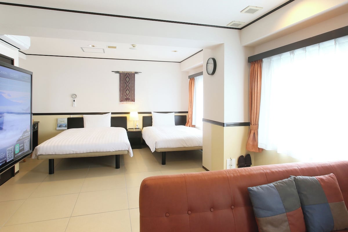 A hotel room with two beds, a TV, a clock, and a window with curtains.