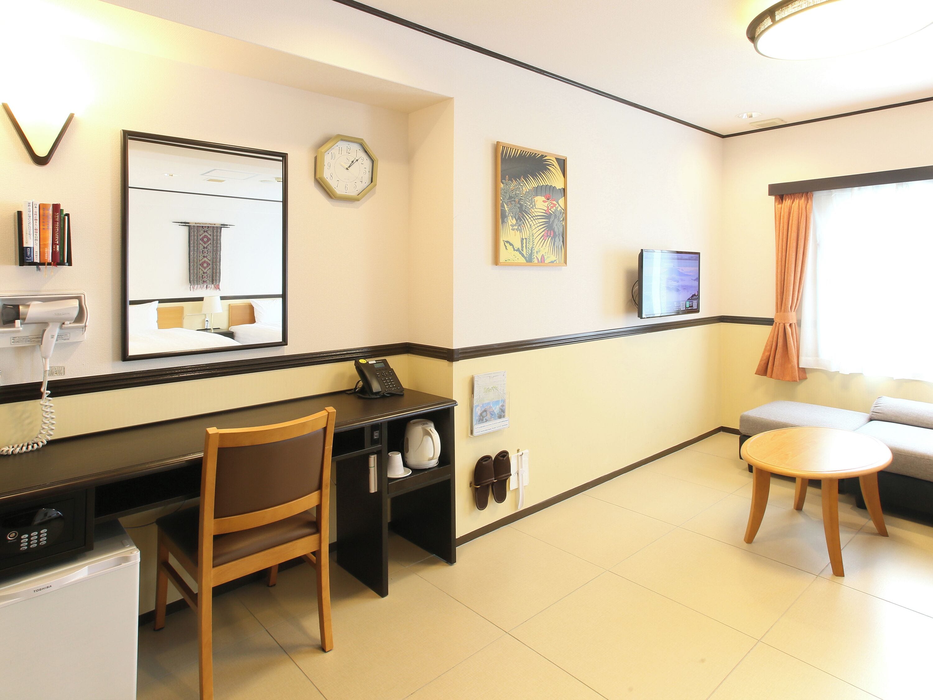 A hotel room with a desk, chair, microwave, and a TV.