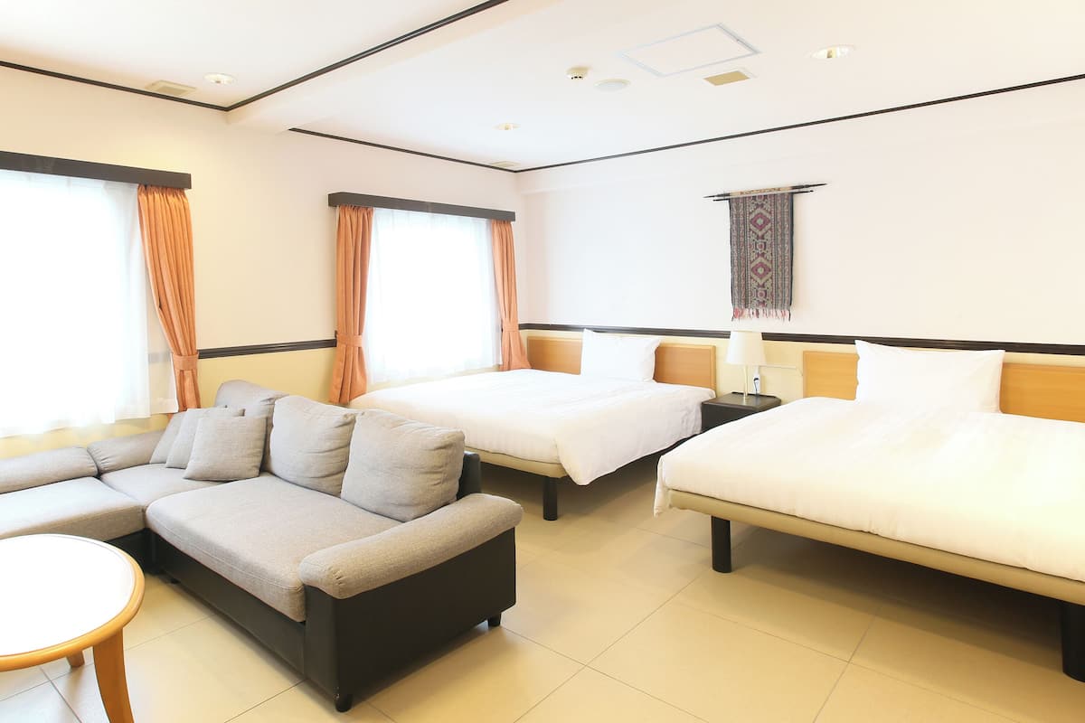 A hotel room with a sofa, two single beds, a small table, and a patterned tapestry on the wall.