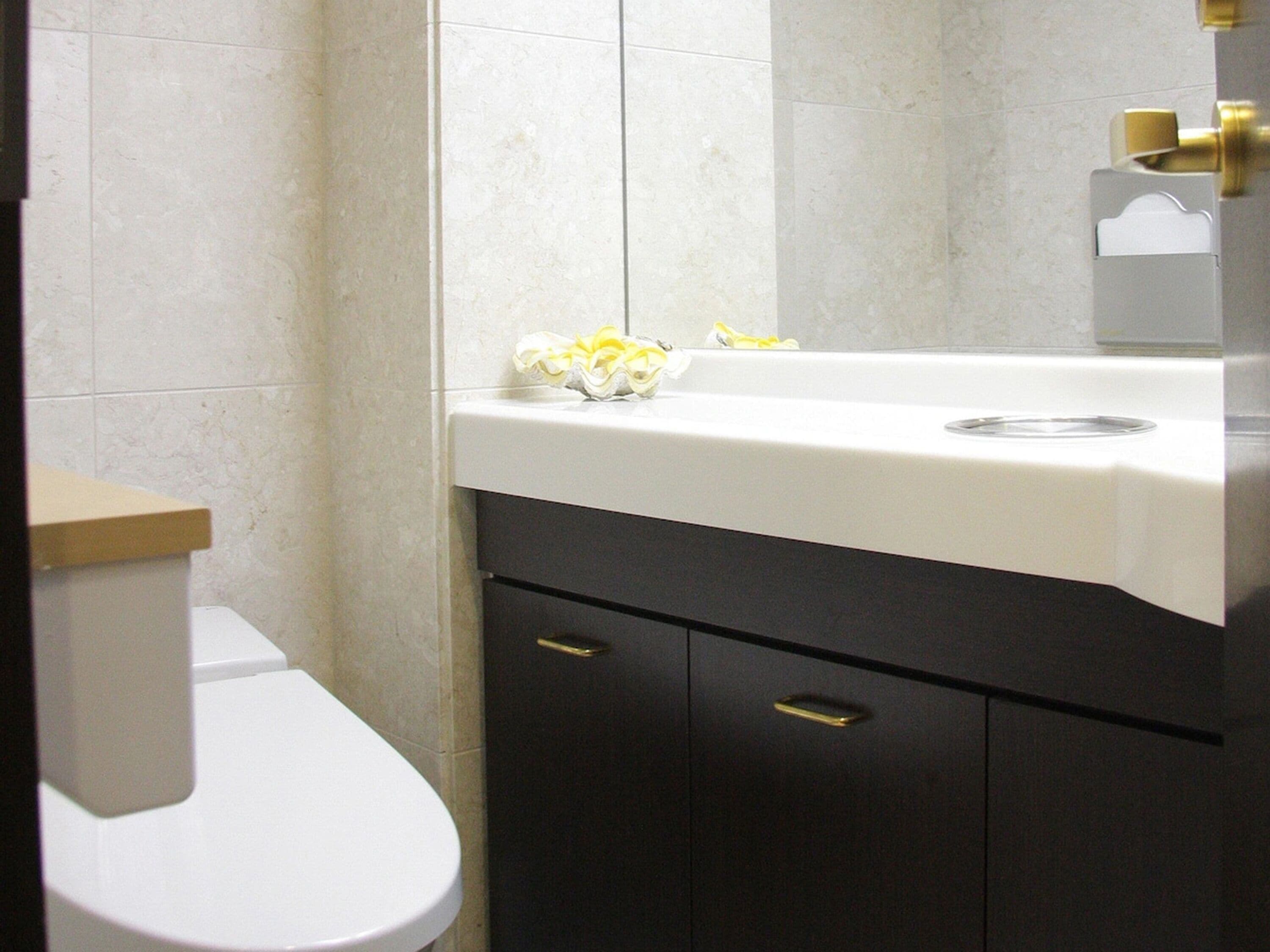 A bathroom with a white toilet, a sink with a white countertop, and a dark cabinet below.