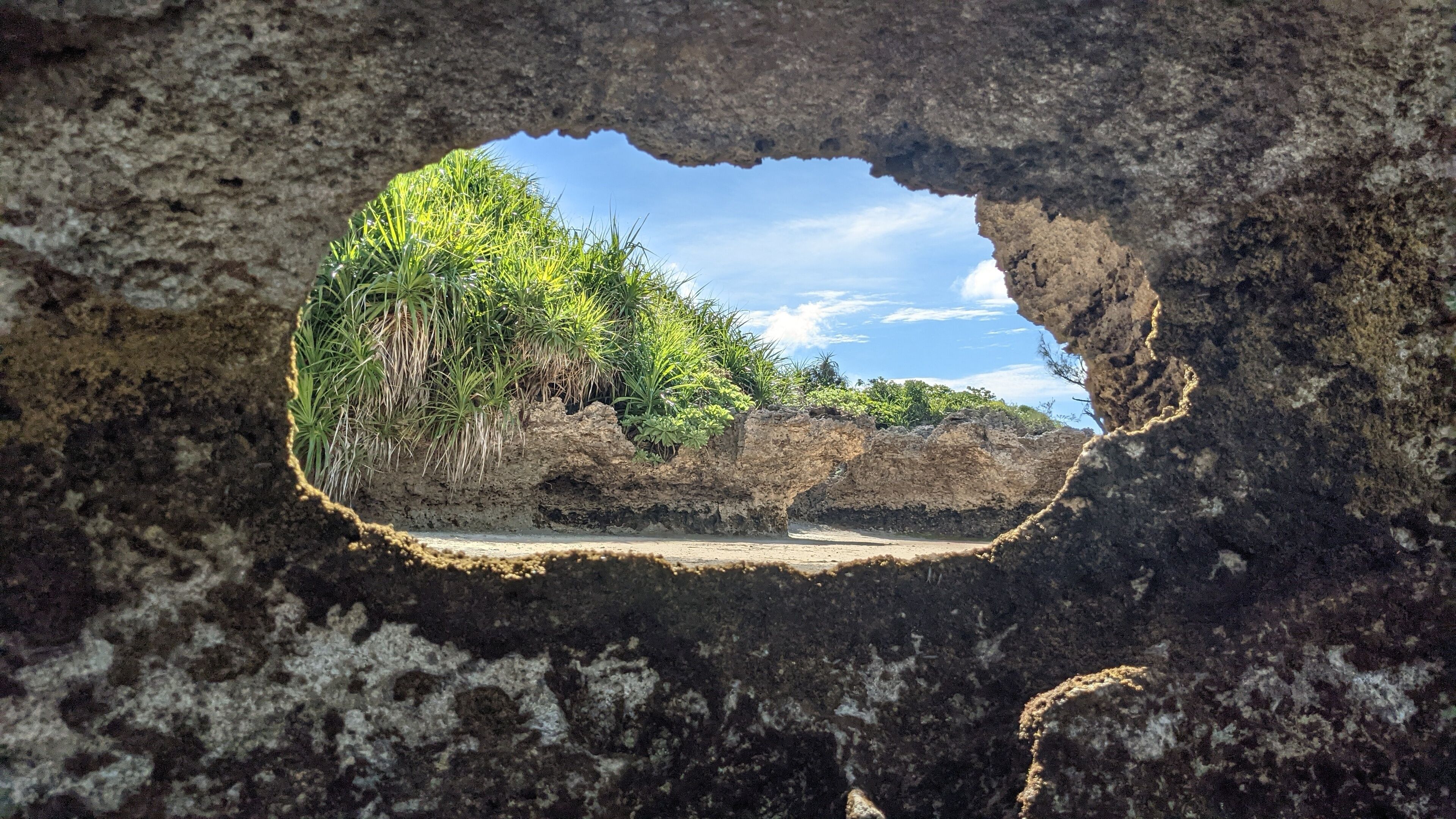 A view through a natural rock opening, revealing a lush green landscape with a clear sky.