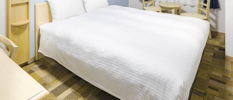 Hotelkamer met een groot bed, een bureau, een stoel, een klein tafeltje en een raam met gordijnen.