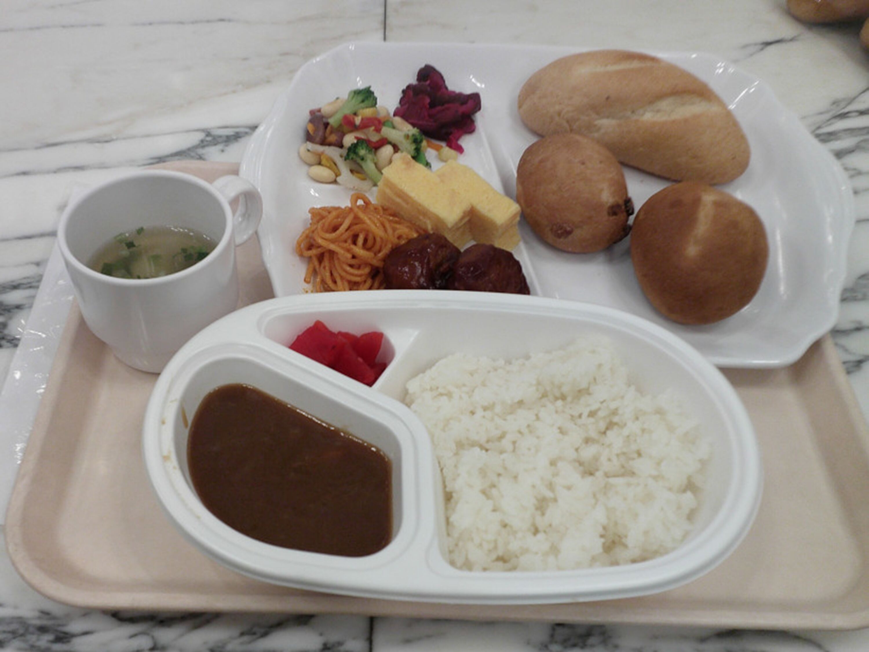 A tray with a variety of food items including rice, soup, bread, and vegetables.