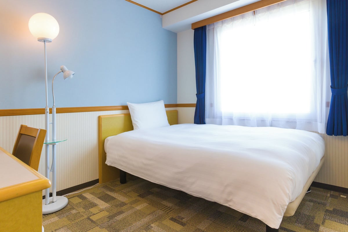 A hotel room with a bed, a desk, a lamp, and a window with curtains.