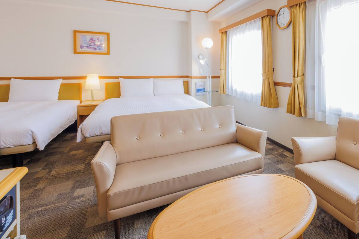A hotel room with two beds, a sofa, a chair, and a round table.
