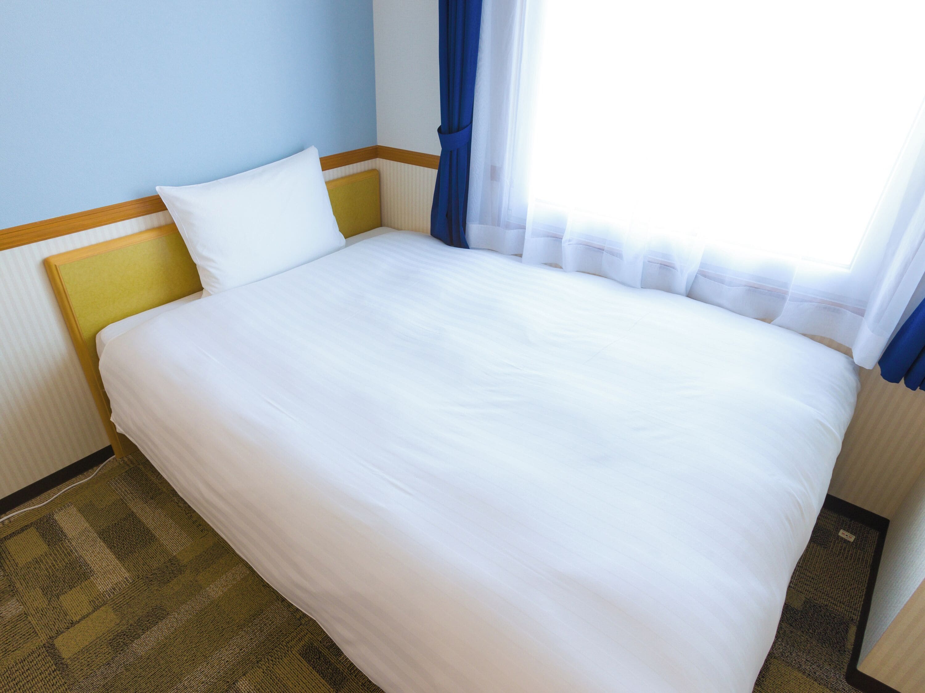 Una cama bien hecha con sábanas blancas, cabecera de madera y alfombra estampada.
