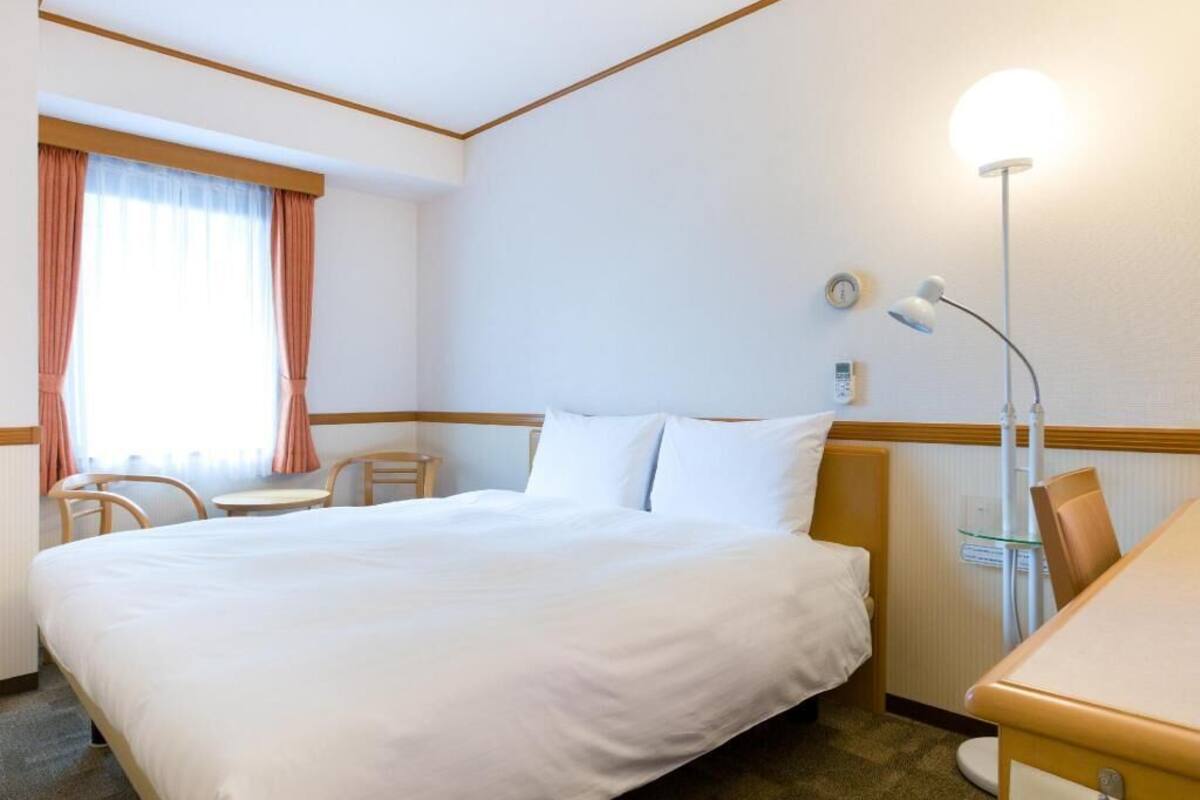 A hotel room with a large bed, a desk, a chair, a lamp, and a window with curtains.