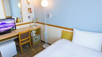 A hotel room with a bed, a desk with a computer, a chair, a desk lamp, a telephone, and a mirror.