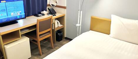 Une chambre d’hôtel équipée d’un lit, d’un bureau, d’une chaise et d’un petit réfrigérateur.