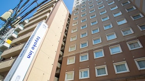 A multi-story building with a beige facade and a brown facade. There are multiple windows on each floor, and a sign with Japanese characters is visible on the beige facade. - Toyoko Inn Kagoshima Chuo Station Nishi (Kagoshima)