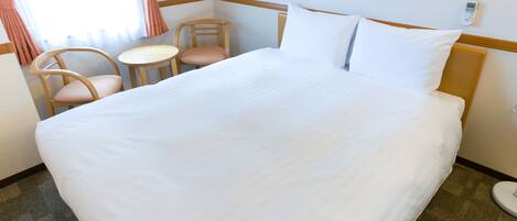A hotel room with a large bed, two chairs, a small table, and a thermostat on the wall.