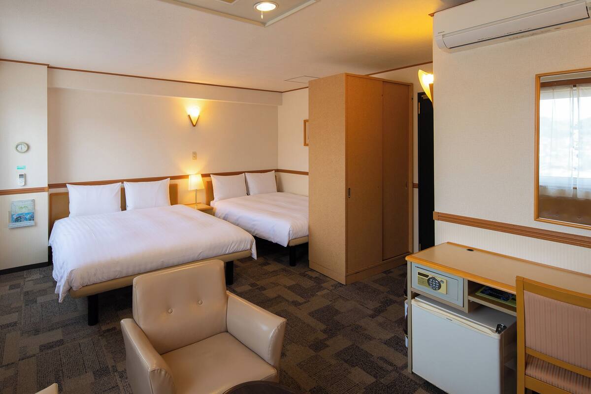 A hotel room with two beds, a desk, a chair, and a minibar.