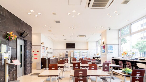 A modern restaurant with a clean, spacious interior, featuring a long counter with seating, a kitchen area, and large windows providing natural light. - Toyoko Inn Kagoshima Chuo Station Nishi (Kagoshima)