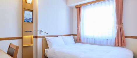 A hotel room with a bed, a desk, a chair, a wall-mounted lamp, and a window with curtains.