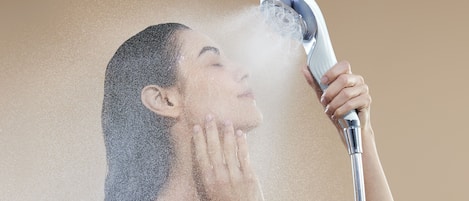 A person using a handheld showerhead, with water spraying around them.