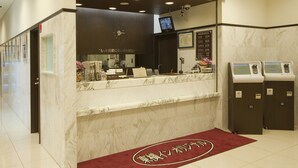A reception area with a marble counter, a clock, a television, and two self-service kiosks.