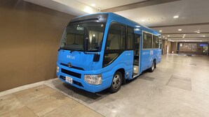 Een blauwe bus geparkeerd in een ruime, overdekte parkeergarage met betegelde vloer en hoge plafonds.