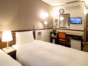 Une chambre d’hôtel comprenant un lit, un bureau avec une chaise, une lampe de bureau, un sèche-cheveux, une horloge et un téléviseur.
