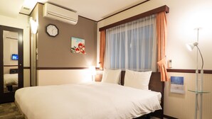 Hotelkamer met een groot bed, een klok aan de muur, een schilderij, een raam met gordijnen en een staande lamp.