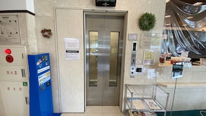 Un ascenseur avec une porte en verre, un distributeur automatique bleu et un petit présentoir à magazines.