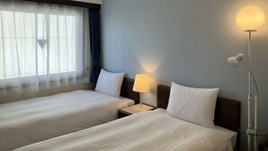 Une chambre d’hôtel avec deux lits, une table de chevet, une lampe et une fenêtre avec des rideaux.
