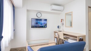 Ein Hotelzimmer mit Bett, Schreibtisch, Stuhl, Fernseher, einer Uhr und einem Spiegel.