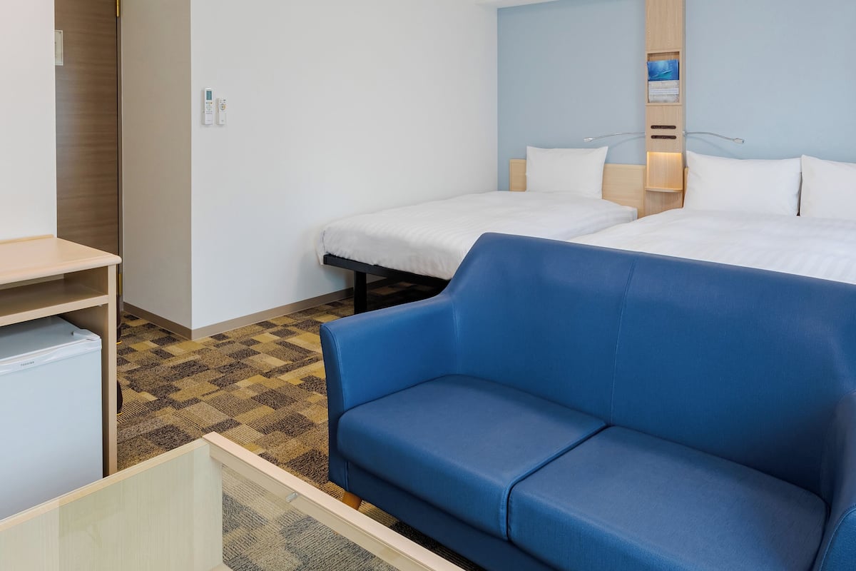 Une chambre d’hôtel avec deux lits, un canapé bleu, un petit bureau et une moquette à motifs.