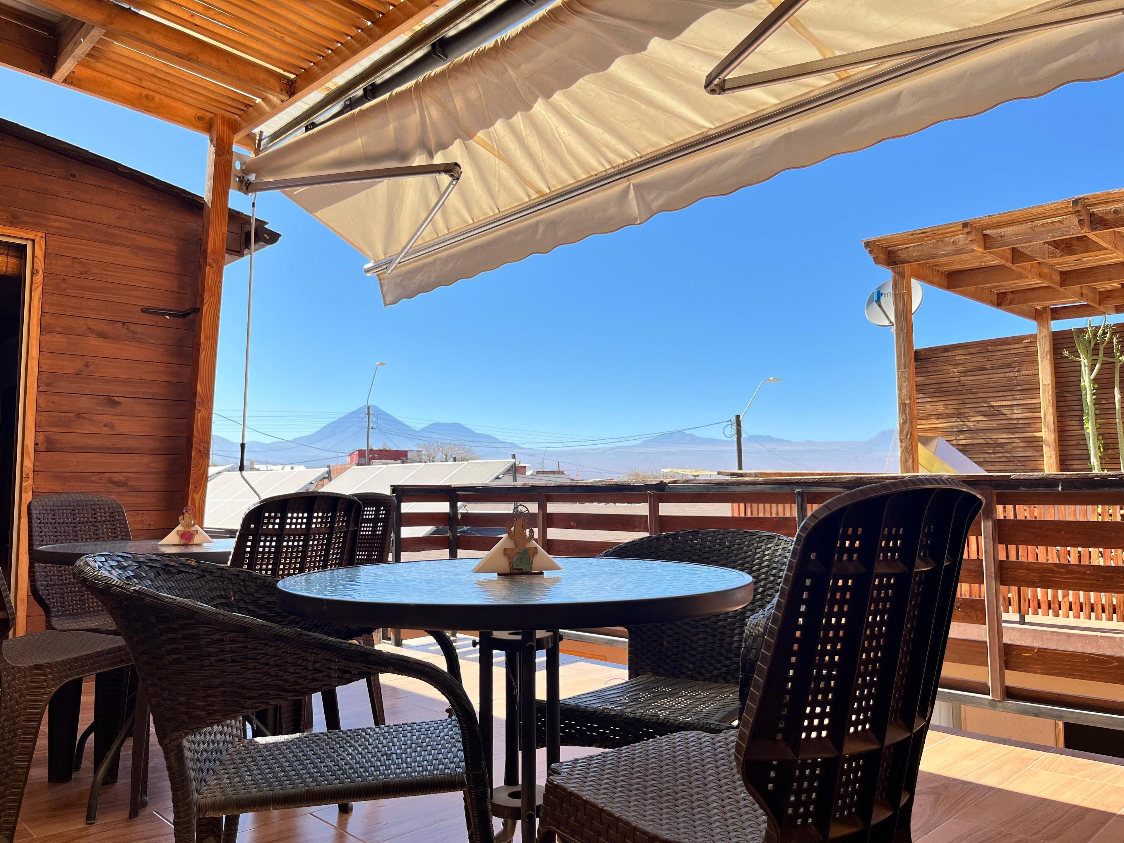 A wooden deck with wicker chairs and a round table, overlooking a mountainous landscape.