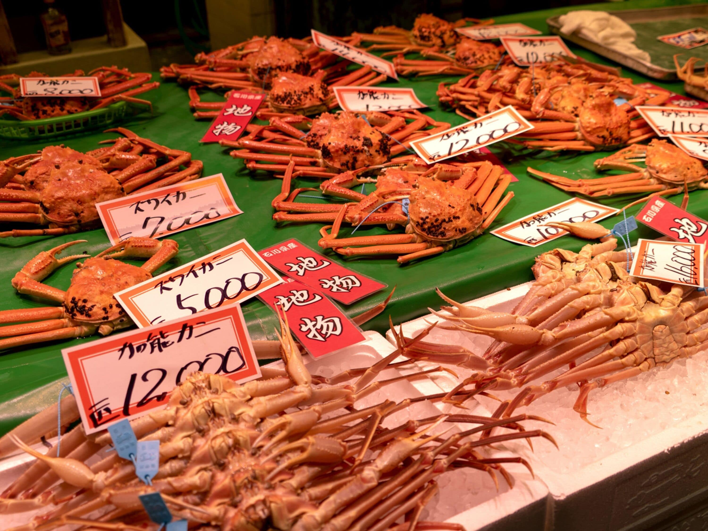 A seafood market with various types of crabs and prawns displayed on ice, each with a price tag.