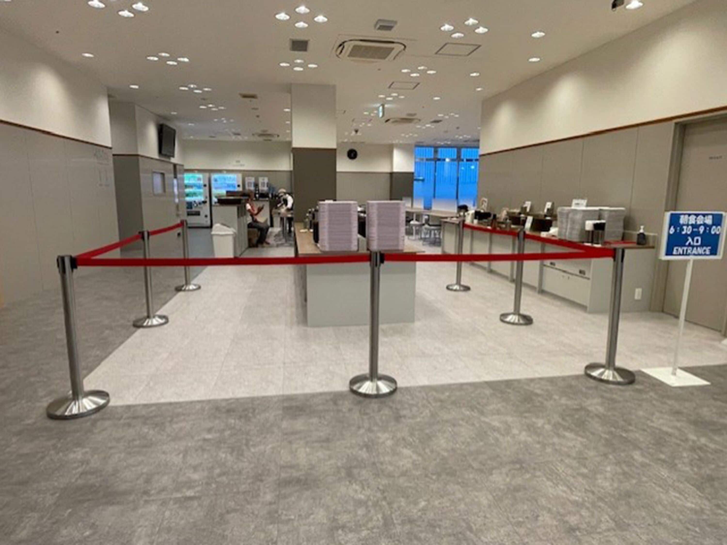 A hotel reception area with a red rope barrier, a blue entrance sign, and a counter with a computer monitor.