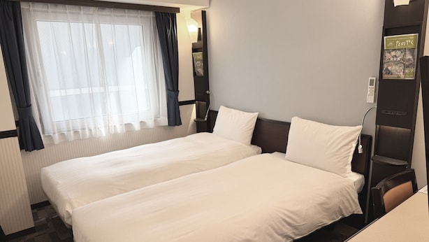 A hotel room with two beds, a window with curtains, a bedside table, a lamp, and a wall-mounted shelf with books. - Toyoko Inn Tokyo Ueno Tawaramachi-eki (Tokyo)