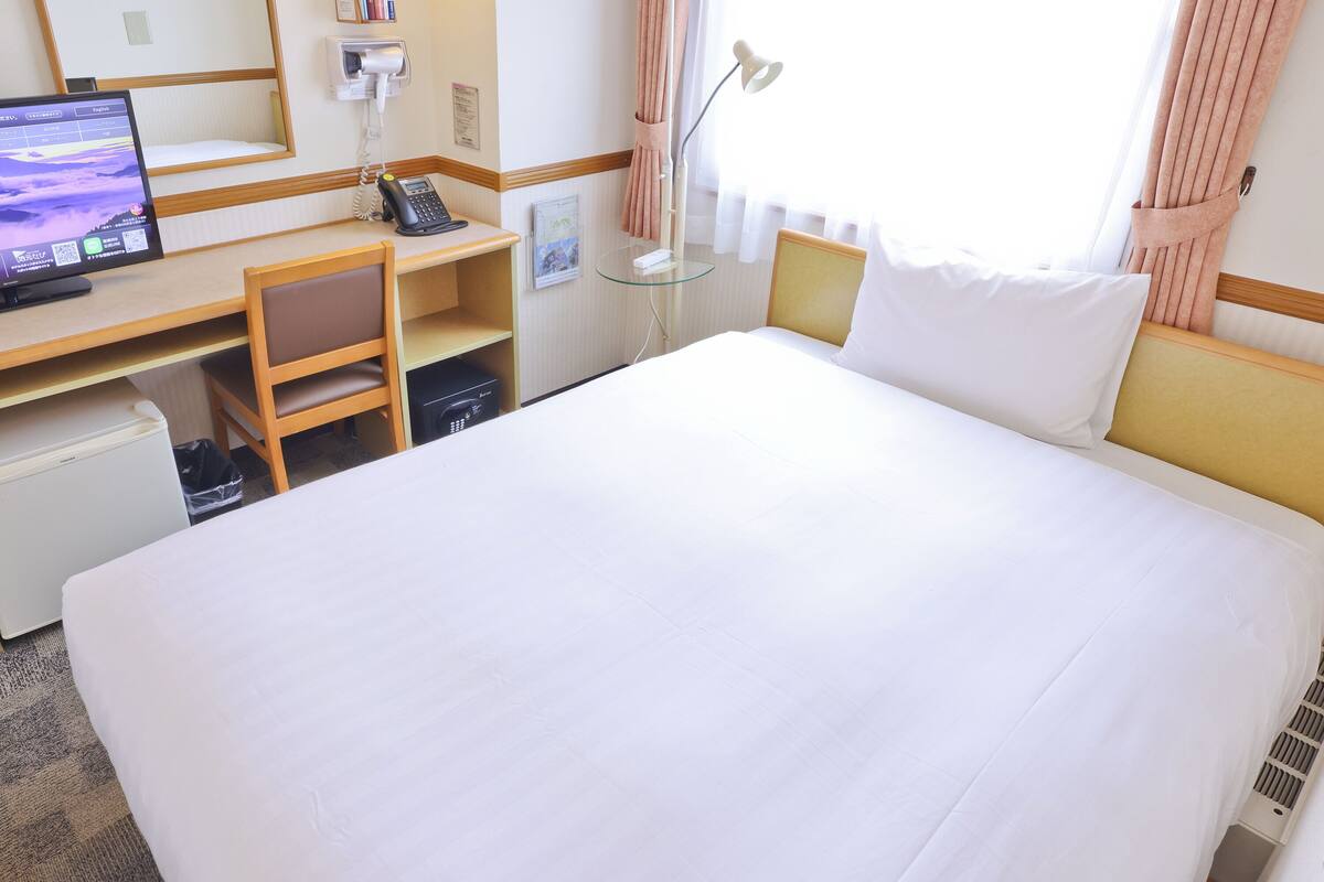 Een hotelkamer met een groot bed, een bureau met een computer, een telefoon en een kleine koelkast.