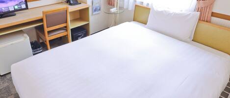 A hotel room with a large bed, a desk with a computer, a telephone, and a small refrigerator.