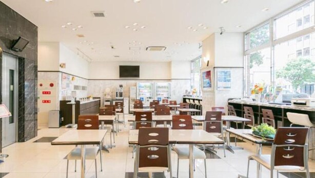 A modern restaurant interior with multiple tables and chairs, a kitchen area, and large windows providing natural light. - Toyoko Inn Shimonos Station Kaikyo Yume Tower Mae (Shimonoseki)