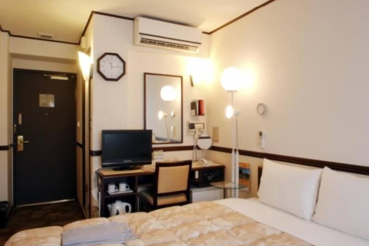 Een hotelkamer met een bed, een televisie, een bureau met een computer, een spiegel en een airconditioning.