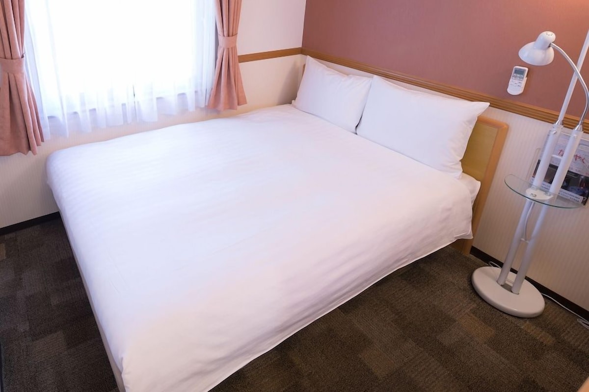 Ein ordentlich bezogenes Bett in einem Hotelzimmer mit Nachttischlampe und Wandtelefon.