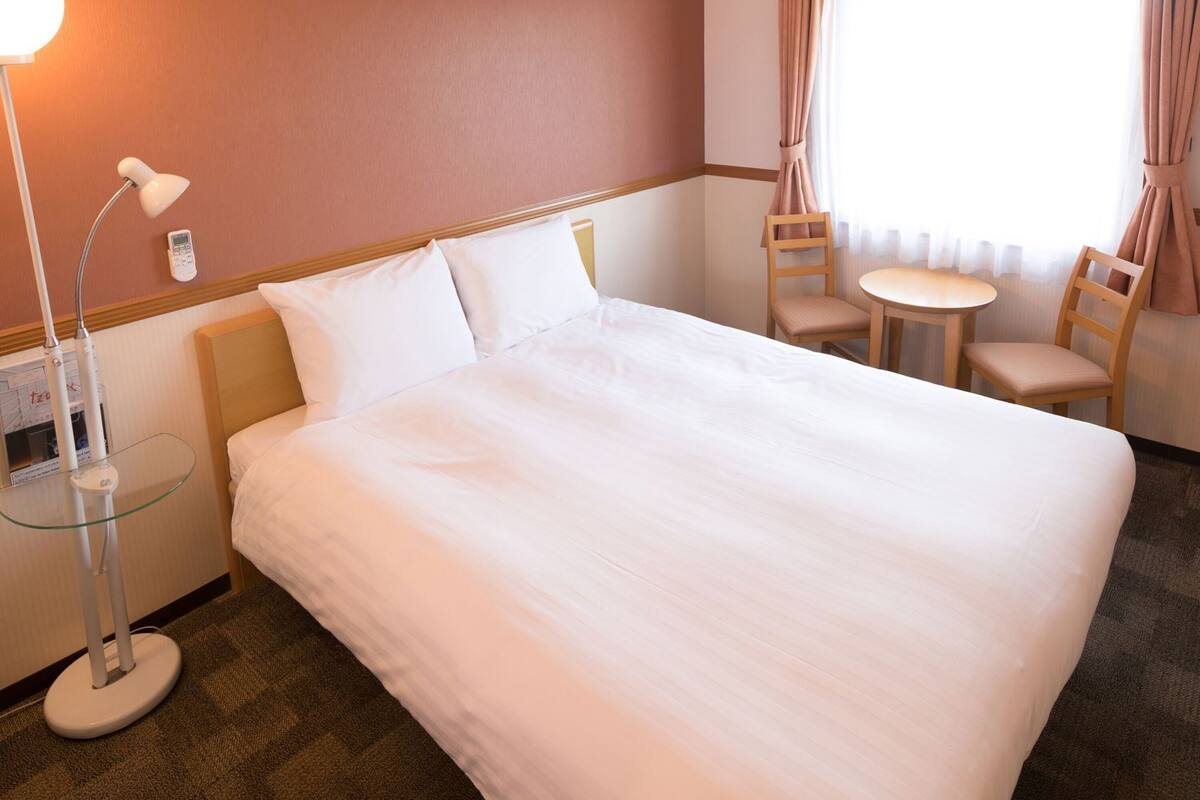 Une chambre d’hôtel avec un grand lit, une lampe de chevet, une petite table avec des chaises et une fenêtre avec des rideaux.