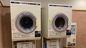 Deux machines à laver à chargement frontal dotées de panneaux de commande, un sèche-linge fixé au mur et une poubelle.