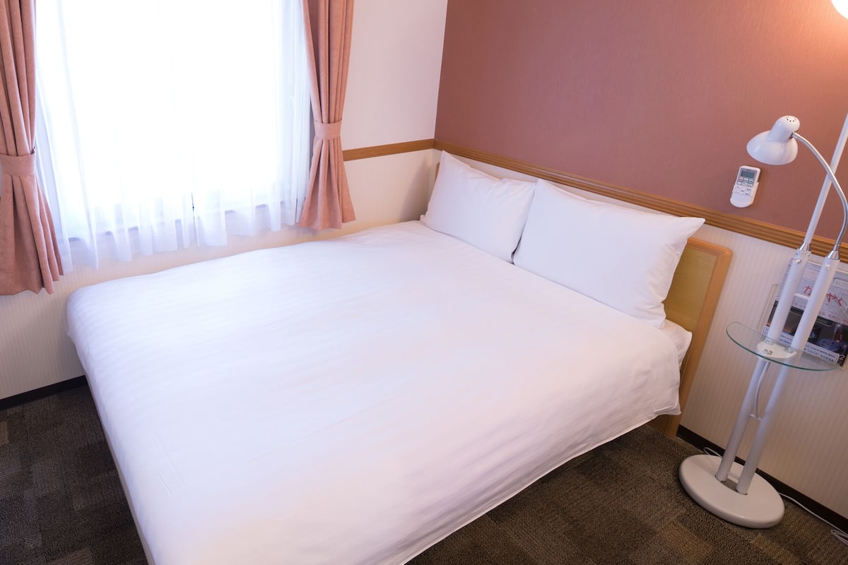 Un lit bien fait dans une chambre d’hôtel, avec une lampe de chevet et un panneau de commande au mur.
