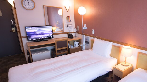 Hotelkamer met een bed, een bureau met computer, een stoel, een lamp en een klok aan de muur.