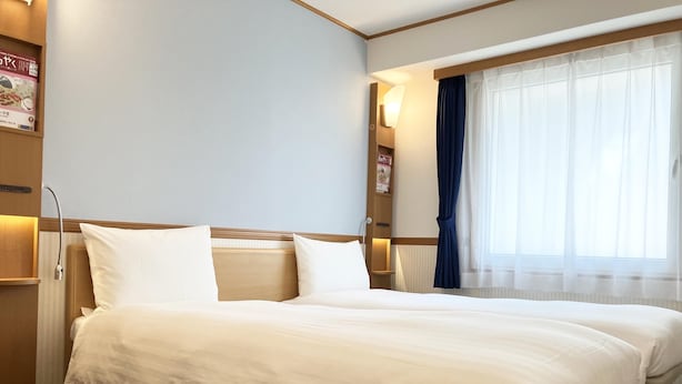 A hotel room with a large bed, a bedside table, a lamp, and a window with curtains. - Toyoko Inn Tokyo Station Shin Ohashi Mae (Tokyo)