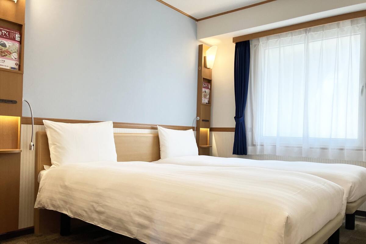 Ein Hotelzimmer mit einem großen Bett, einem Nachttisch, einer Lampe und einem Fenster mit Vorhängen.
