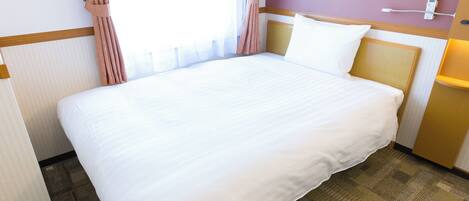 A hotel room with a large bed, a bedside table, a lamp, and a window with curtains.
