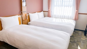 Habitación de hotel con dos camas, una mesita de noche, una lámpara y una ventana con cortinas.
