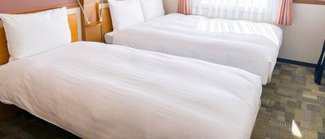 A hotel room with two beds, a nightstand, a lamp, and a window with curtains.