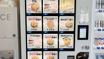 Una macchina distributrice con diverse opzioni alimentari, il cui costo varia fino a 500 yen, tra cui pollo al vapore e dolcetti di riso.