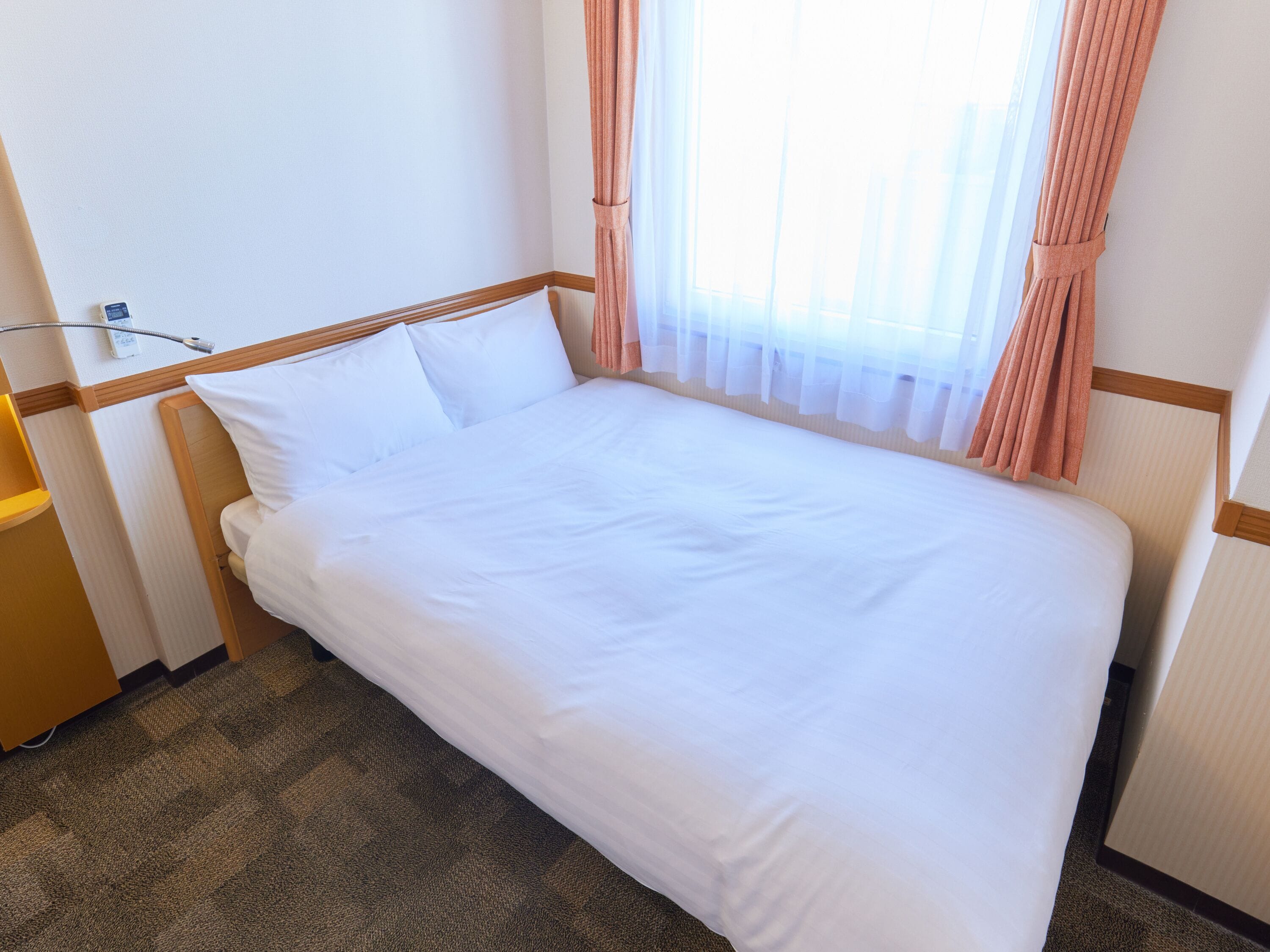 Un lit bien fait, avec du linge de lit blanc, dans une chambre d'hôtel.