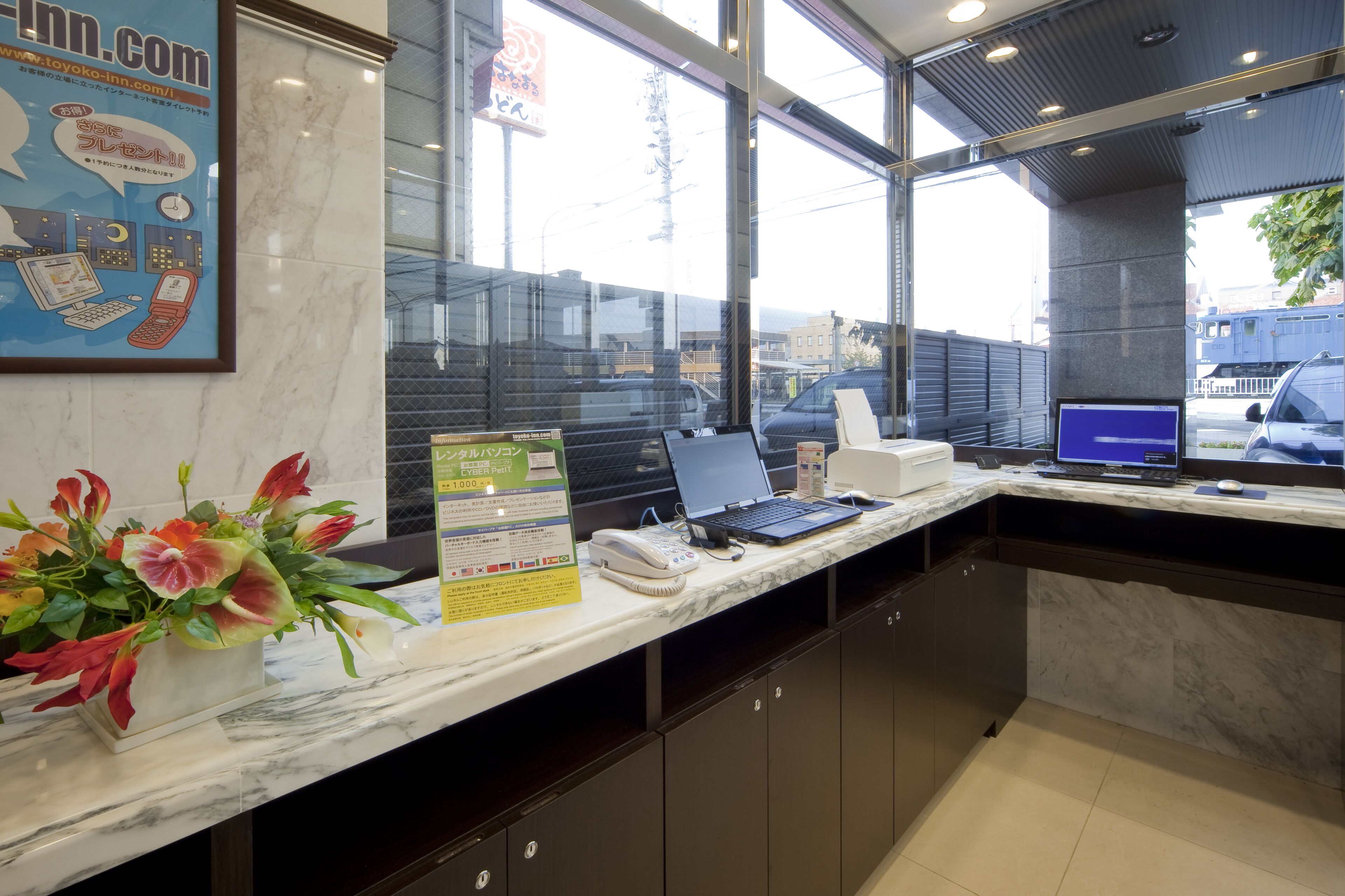 A hotel reception desk with a computer, a phone, and a sign about a 1,000 yen offer.