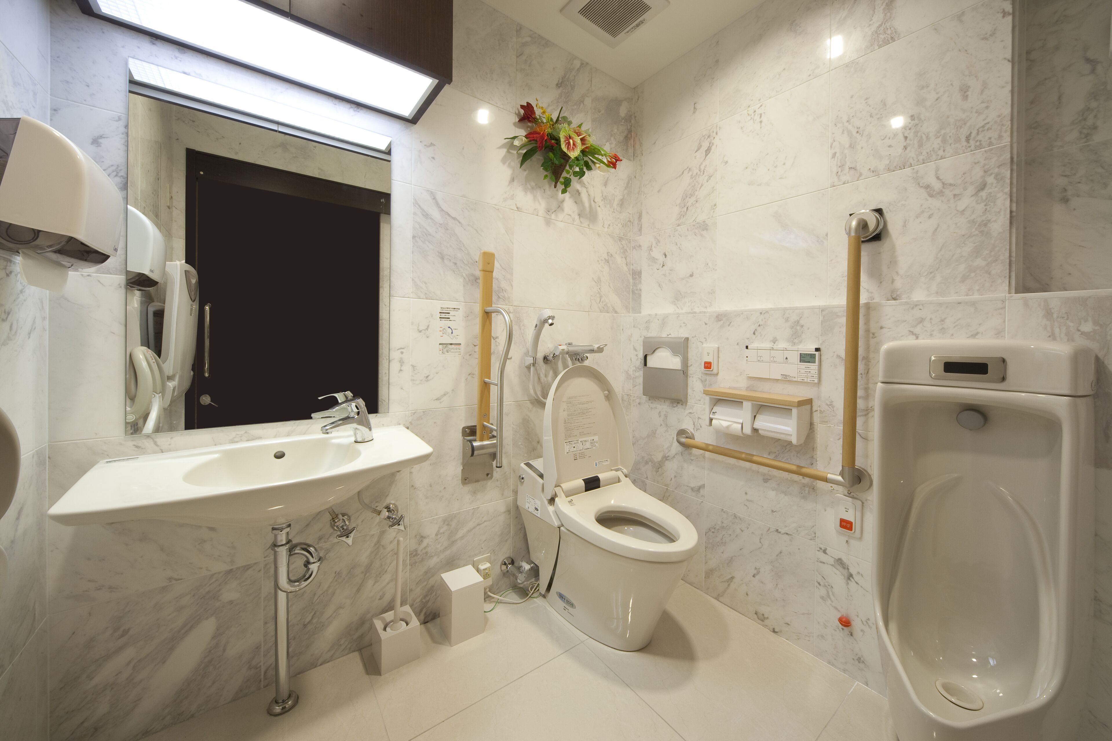 A modern bathroom with a marble sink, a toilet with a handrail, and a urinal.